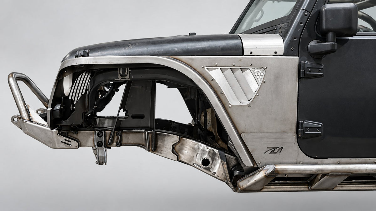 Close-up of the front left side of a silver and black off-road vehicle, showing the wheel well, front bumper guard, fender, and side panel details against a light gray studio background. Motobilt MB1273 Tomahawk Fenders